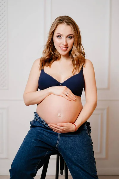 An attractive pregnant woman with a bare tummy sits on a chair. — Stock Photo, Image