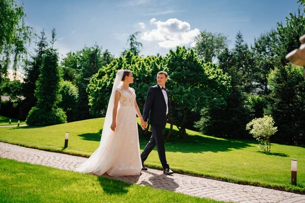 Les mariés marchent en se tenant la main le long du chemin dans le parc. — Photo