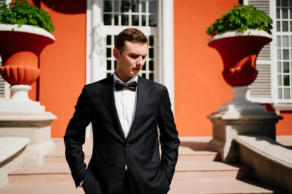 Binanın dışında papyonlu, takım elbiseli somurtkan bir adam.. 