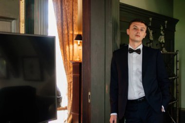  Takım elbiseli, papyonlu bir adam duvarda duruyor.