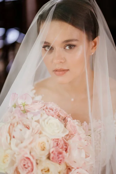 Portré egy gyönyörű menyasszonyról csokorral a fátyol alatt. nőiesség és szépség. — Stock Fotó