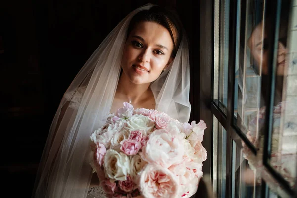 Eine schöne und sanfte Braut in einem dunklen Raum am Fenster. — Stockfoto