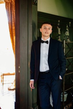  Takım elbiseli, papyonlu bir adam duvarda duruyor.