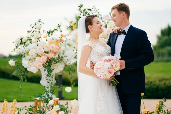 Sposo e sposa nella zona cerimonia nuziale di fiori bianchi e rosa vivi. — Foto Stock