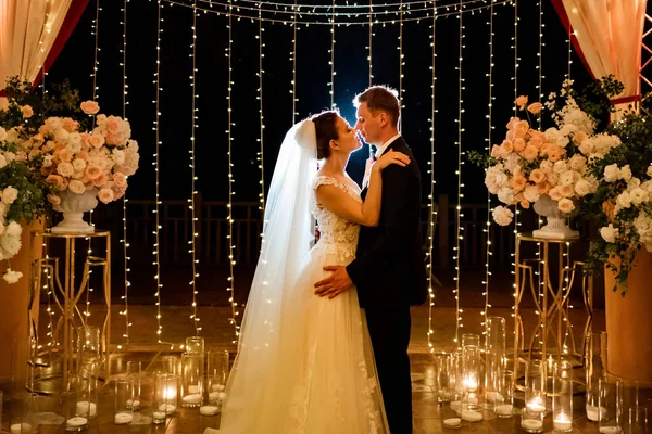 Brautpaar bei Abendhochzeit im Park zwischen Glühbirnen und Girlanden. — Stockfoto