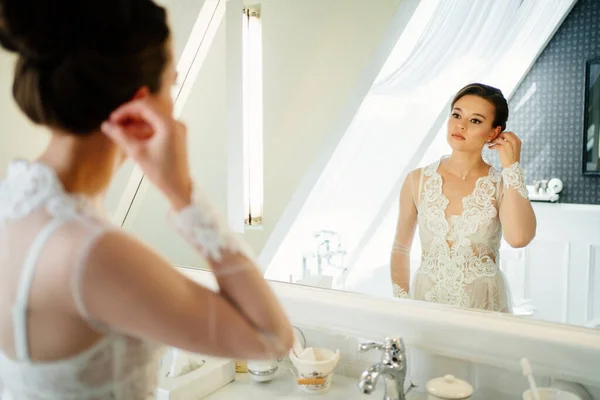 Eine schöne junge Frau in einem Seidenmantel am Spiegel im Badezimmer. — Stockfoto