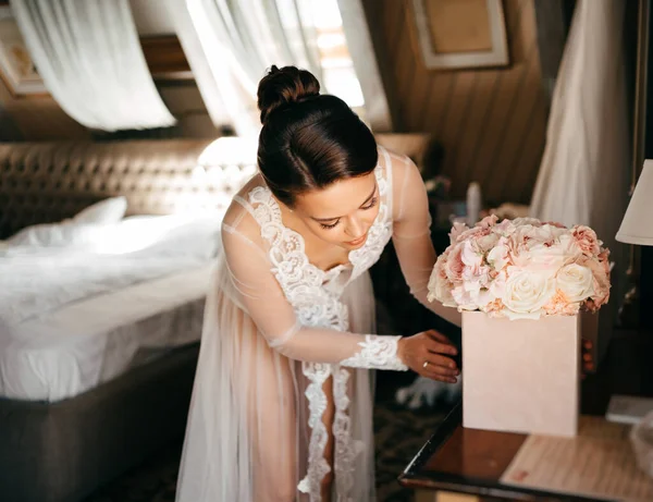 Красива молода жінка в мереживному халаті дивиться на букет квітів в коробці . — стокове фото