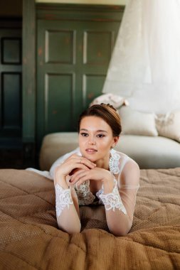 Dantel bornozlu esmer gelin yatakta yatıyor. Düğünden önce sabah.