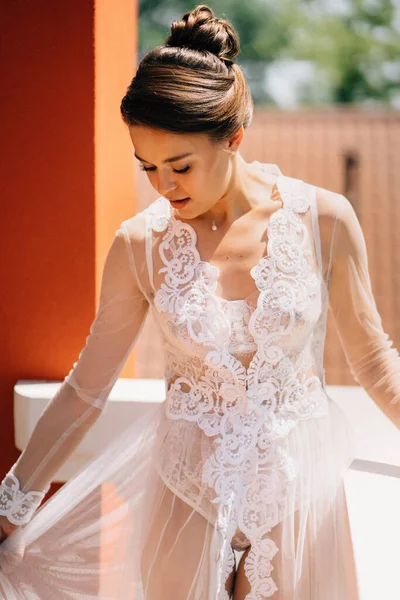 Una hermosa novia en una túnica de encaje transparente se encuentra en la terraza. — Foto de Stock