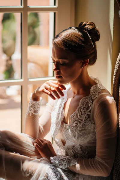 A beautiful and gentle woman in a sexy lace robe sits by the window. — Stock Photo, Image