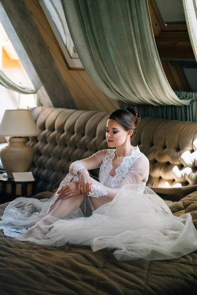 Una novia con una bata de encaje sentada en la cama. mañana antes de la boda. — Foto de Stock