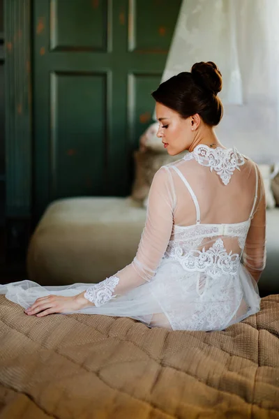 Vista desde atrás. novia con túnica de encaje sentada en la cama. mañana antes de la boda. — Foto de Stock