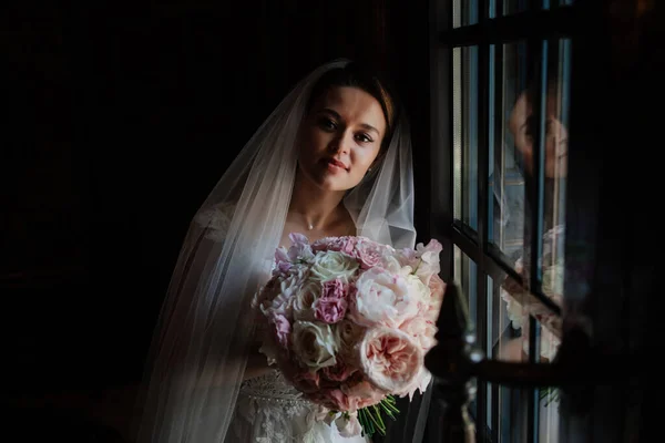 Une belle et douce mariée dans une pièce sombre près de la fenêtre. — Photo