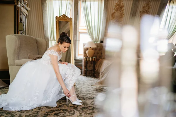 Eine schöne Braut in einem weißen Kleid zieht Schuhe an. Hochzeitsmode. — Stockfoto