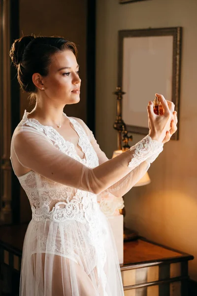 Een mooie jonge vrouw in een kanten mantel met parfum in haar handen. parfumerie — Stockfoto