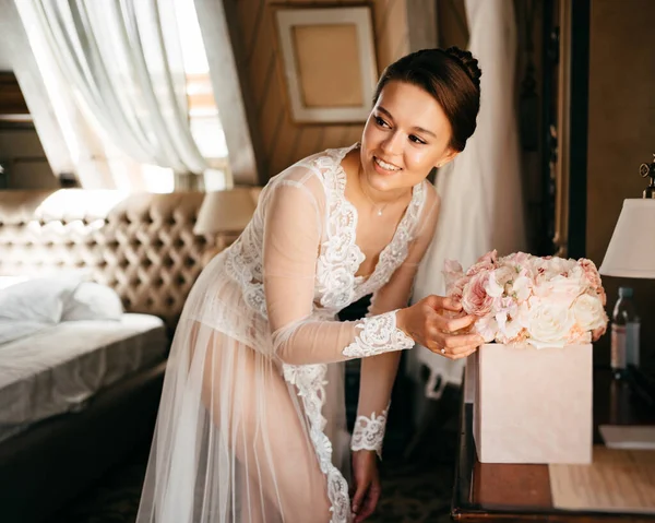 Eine schöne junge Frau im Spitzengewand betrachtet einen Blumenstrauß in einer Schachtel. — Stockfoto