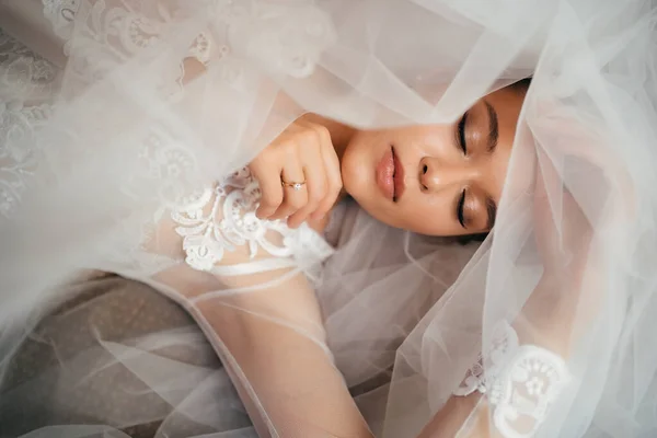 Eine Braut im Spitzengewand liegt auf einem Schleier im Bett. Morgen vor der Hochzeit. — Stockfoto