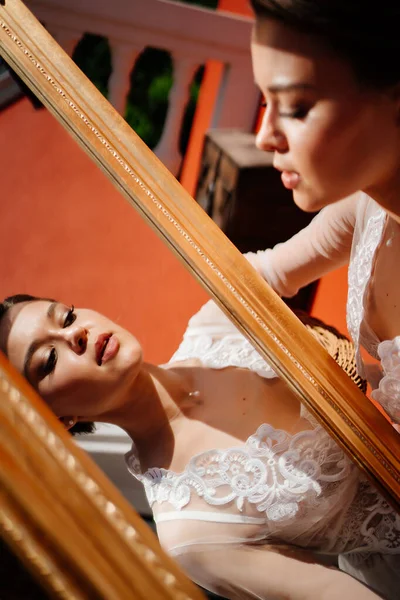 Una hermosa joven con una túnica de encaje mira su reflejo en el espejo. — Foto de Stock