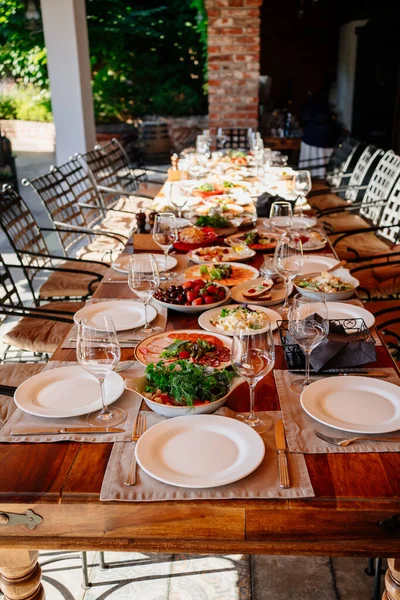 Nagy fa asztal tálalva tányérokkal salátával és harapnivalókkal a nyitott teraszon — Stock Fotó