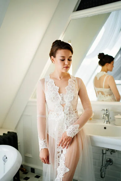 Een mooie jonge vrouw in een zijden badjas door de spiegel in de badkamer. — Stockfoto