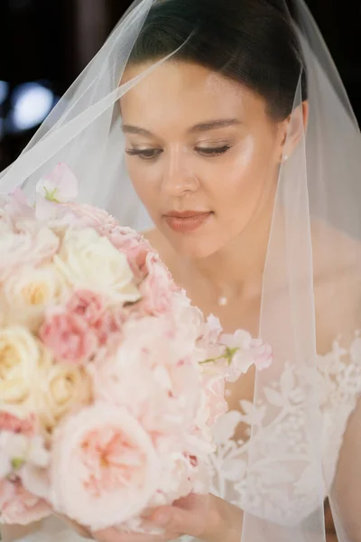 Porträt einer schönen Braut mit Blumenstrauß unter einem Schleier. Weiblichkeit und Schönheit. — Stockfoto