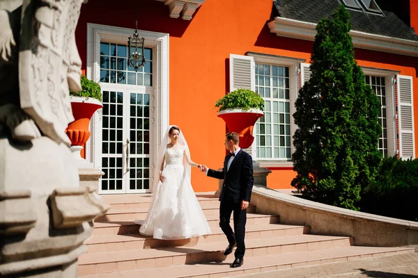 Nevěsta a ženich jdou držet za ruce v krásné budově. — Stock fotografie