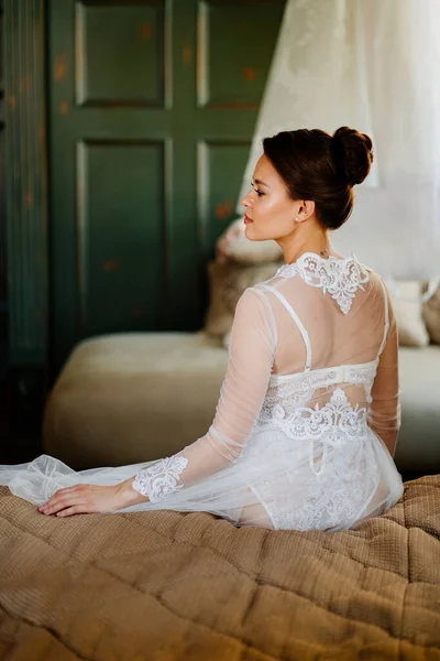 Vista desde atrás. novia con túnica de encaje sentada en la cama. mañana antes de la boda. — Foto de Stock