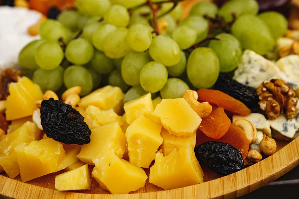 Fromages au raisin, fruits secs, noix, miel et confiture sur une assiette en bois. — Photo