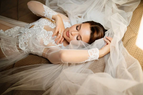 一个穿着花边长袍的温柔的新娘躺在床上，披着面纱。婚礼前的早上. — 图库照片