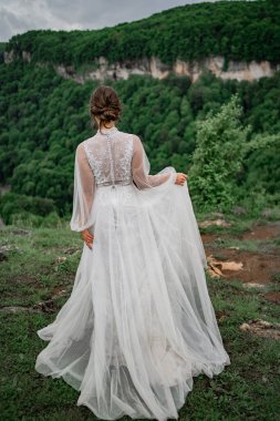 Arkadan bak. Dağlarda poz veren gelinlikli gelin. Gelin kıyafetleri