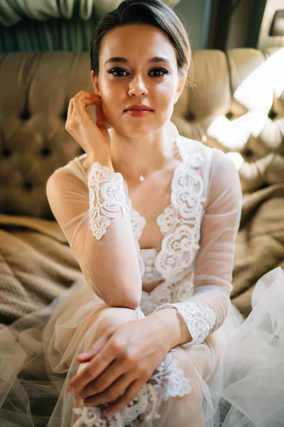 Una novia con una bata de encaje sentada en la cama. mañana antes de la boda. — Foto de Stock