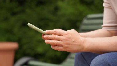 Kadın elinde bir akıllı telefon tutuyor ve yayınları sosyal ağlardan izliyor.