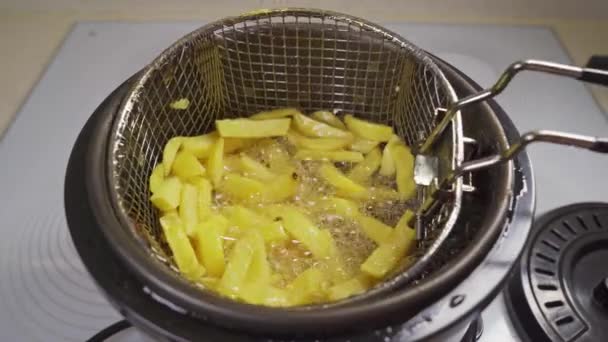 A basket of potatoes is taken out of the deep fryer. cooking french fries — Stock Video