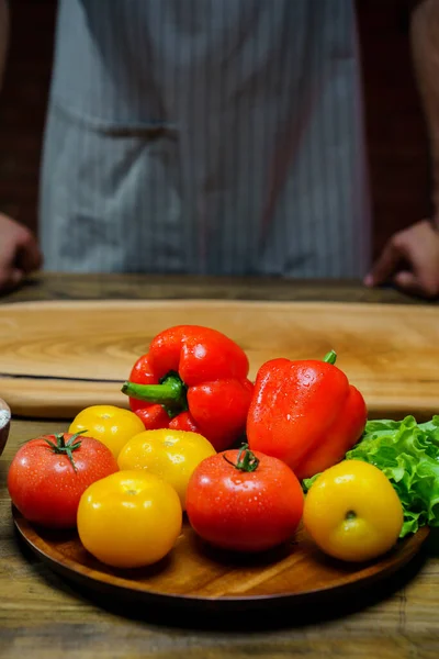 Tomates amarelos e vermelhos, alface e pimentão com gotas de água. homem de avental. — Fotografia de Stock
