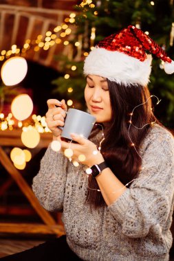 Güzel bir Koreli esmer Noel Baba şapkasıyla kakao içiyor. 
