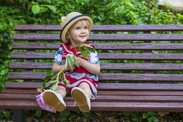 Lindo niño sentado en un banco con una flor — Foto de Stock