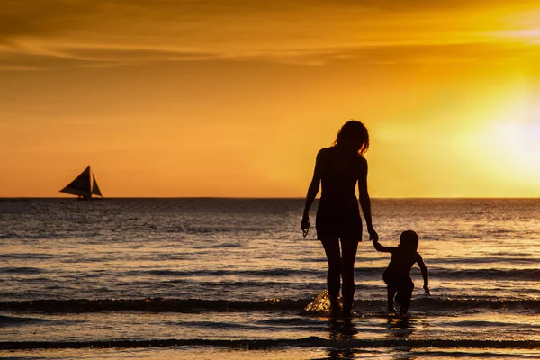 Matka i syn przejść przez fale o zachodzie słońca — Zdjęcie stockowe