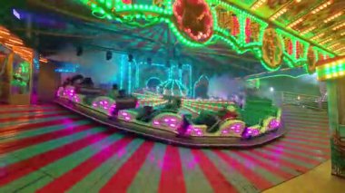 BUDAPEST, HUNGARY NOVEMBER 28, 2025: hızlı dönen bir atlıkarınca bir gece fuarında duman ve yapay sis içinde döner. Uzun pozlama efekti, karanlık gökyüzüne karşı parlak ışıklarla dekore edilmiş lunaparkın hareket bulanıklığını gösteriyor..