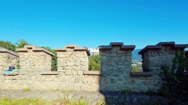 SALZBURG, AUSTRIA ECTOBER 03, 2025: Bir tepenin üzerinde oturan uzak Hohensalzburg Kalesi 'ne doğru Josefsturm' un taş siperlerinden bir manzara. Sahne, açık mavi gökyüzüne karşı savunma duvarının tarihi yapısını vurguluyor..