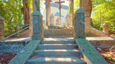 SALZBURG, AUSTRIA ECTOBER 3, 2025: Taş heykeller ve üç ahşap haçın yer aldığı dini bir anıtın düşük açılı görüntüsü. Site, yemyeşil ağaçlar ve parlak, berrak bir gökyüzünün altında sonbahar yapraklarıyla bir yamaçta yer alıyor..