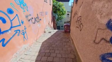 SALZBURG, AUSTRIA 3 Ekim 2025: Dar bir yaya geçidinde tarihi binalar arasında taş merdivenler ve kaldırımlar bulunur. Yan duvarlar çeşitli renkli duvar yazıları ve sokak sanatı ile aydınlık gün ışığında süslenmiş..