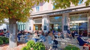 SALZBURG, AUSTRIA ECTOBER 03, 2025: Müşteriler güneşli bir sonbahar gününde tarihi Cafe Bazar 'ın açık masalarında otururlar. Sahne, nehir kenarındaki ağaçların gölgesinde dinlenen insanların olduğu klasik bir Avrupa kafe kültürünü gösteriyor..