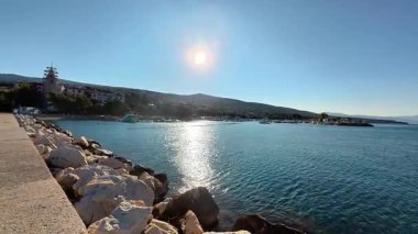 Hırvatistan 'ın Crikvenica kentindeki taştan bir rıhtımdan mavi Adriyatik Denizi' nin gündüz manzarası. Parlak gün ışığı, temiz bir gökyüzünün altında su yüzeyini ve kıyı ufkunu aydınlatır..