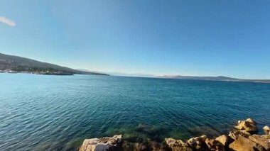 Mavi Adriyatik Denizi 'nin gündüz manzarası ve Hırvatistan' ın Crikvenica kentindeki kıyı şeridinin kıyı ufku. Parlak güneş ışığı kayalık bir toprak setinin yakınındaki su yüzeyine yansıyor..