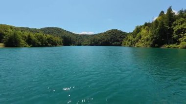 Plitvice Gölleri Ulusal Parkı 'ndaki kristal berrak turkuaz Kozjak Gölü' nün geniş bir manzarası. Bereketli yeşil orman dağları, parlak mavi bir yaz gökyüzünün altında, suyun etrafını sarar..