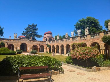 Açık mavi gökyüzünün altındaki tarihi Bory Castle bahçesinde taş heykellerin ve kemerli geçitlerin geniş bir görüntüsü.