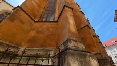 Yıpranmış turuncu taş duvarların alçak açılı manzarası ve tarihi Gotik katedralin uzun boyalı camları. Heybetli mimari, temiz mavi gökyüzüne karşı minderlere ve karmaşık duvarlara sahiptir..