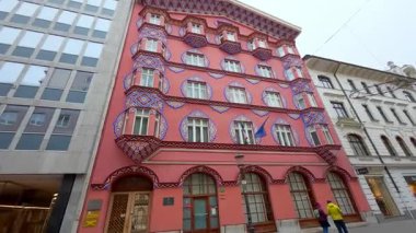 Slovenya 'nın Ljubljana kentindeki ünlü Vurnik Evi, ulusal renklerde geometrik desenlerle süslenmiş canlı pembe bir cephe sergiliyor. Bu Secessionist stil bina dekoratif resimler ve dekoratif pencereler içerir.