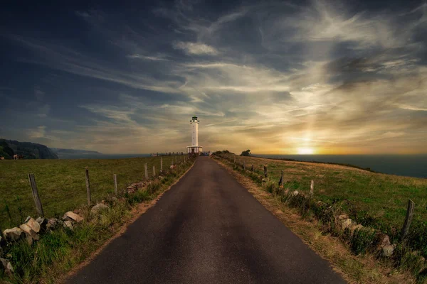 you can see a lighthouse and a road with vegetation and a blue sky with warm clouds