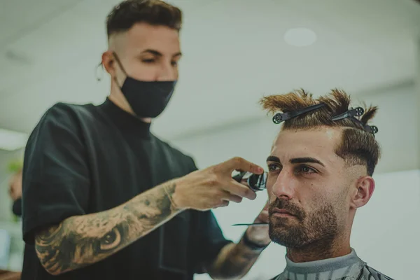 a young man with tattooed arms cuts a man\'s hair in a barbershop